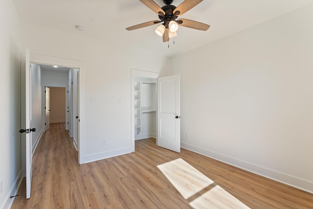 unfurnished bedroom with ceiling fan, a closet, a spacious closet, and light hardwood / wood-style flooring