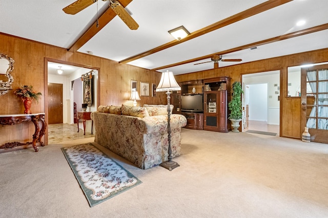 carpeted living room featuring ceiling fan, beamed ceiling, and wood walls