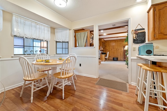 dining space featuring crown molding, wooden walls, light hardwood / wood-style flooring, and a textured ceiling