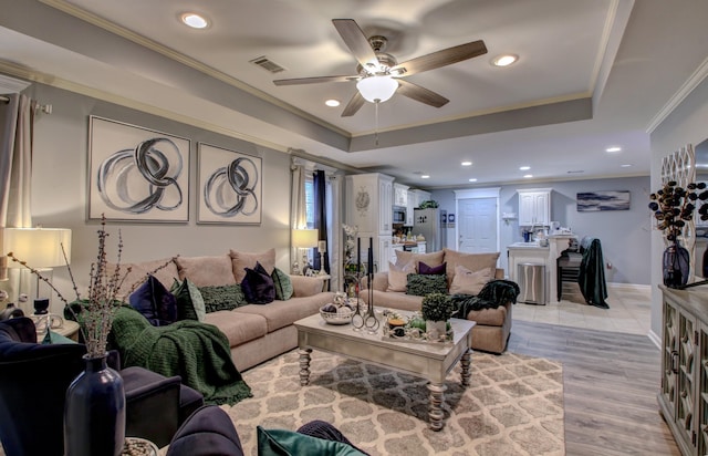 living room featuring a raised ceiling, crown molding, ceiling fan, and light hardwood / wood-style floors