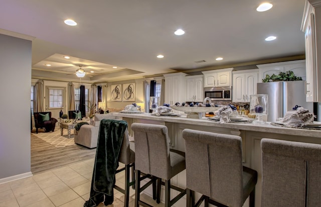 kitchen with appliances with stainless steel finishes, white cabinets, a kitchen bar, ornamental molding, and kitchen peninsula