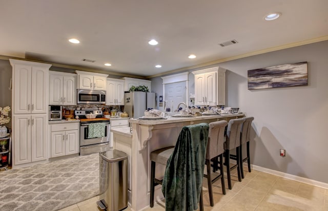 kitchen with appliances with stainless steel finishes, a kitchen breakfast bar, ornamental molding, white cabinets, and kitchen peninsula