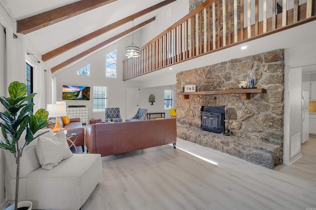 living room featuring light hardwood / wood-style flooring, high vaulted ceiling, beamed ceiling, and a wood stove