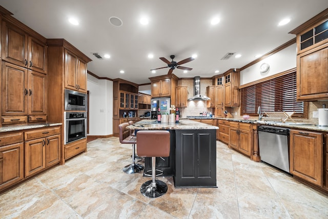 kitchen featuring light stone counters, wall chimney range hood, stainless steel appliances, and a center island