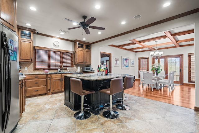 kitchen with stainless steel refrigerator, hanging light fixtures, a kitchen island, light stone counters, and a kitchen bar