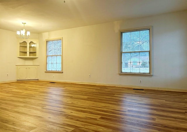 unfurnished living room featuring hardwood / wood-style flooring, a wealth of natural light, and a chandelier