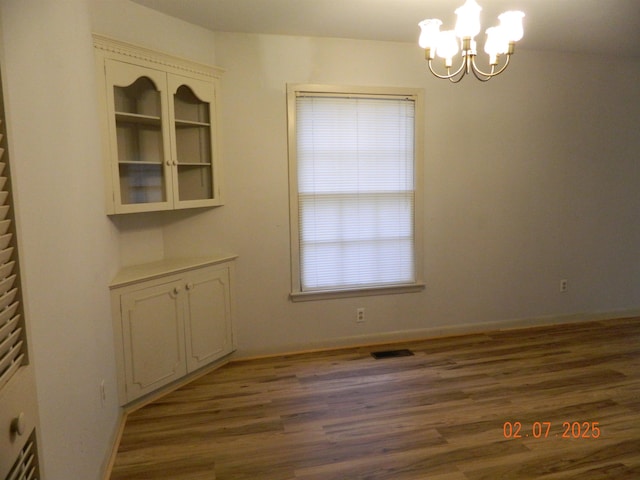 unfurnished dining area with dark wood-type flooring and an inviting chandelier