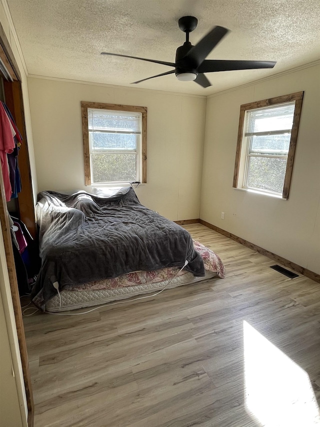 bedroom featuring ornamental molding, light hardwood / wood-style floors, multiple windows, and a textured ceiling