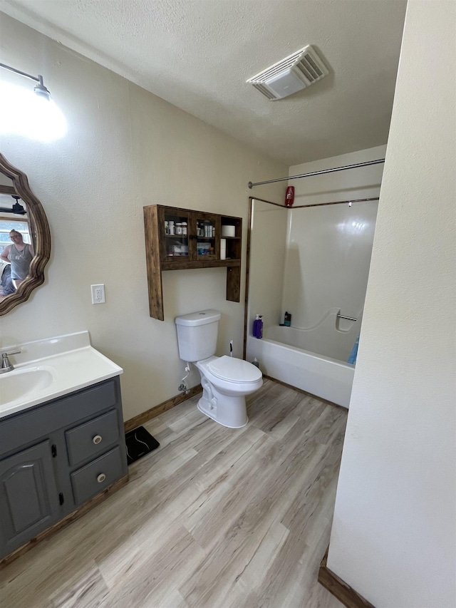 full bathroom featuring hardwood / wood-style flooring, shower / bathing tub combination, vanity, a textured ceiling, and toilet