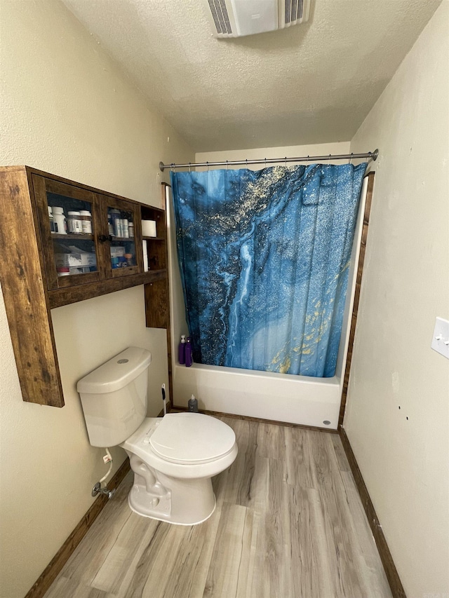 bathroom featuring shower / tub combo with curtain, wood-type flooring, toilet, and a textured ceiling