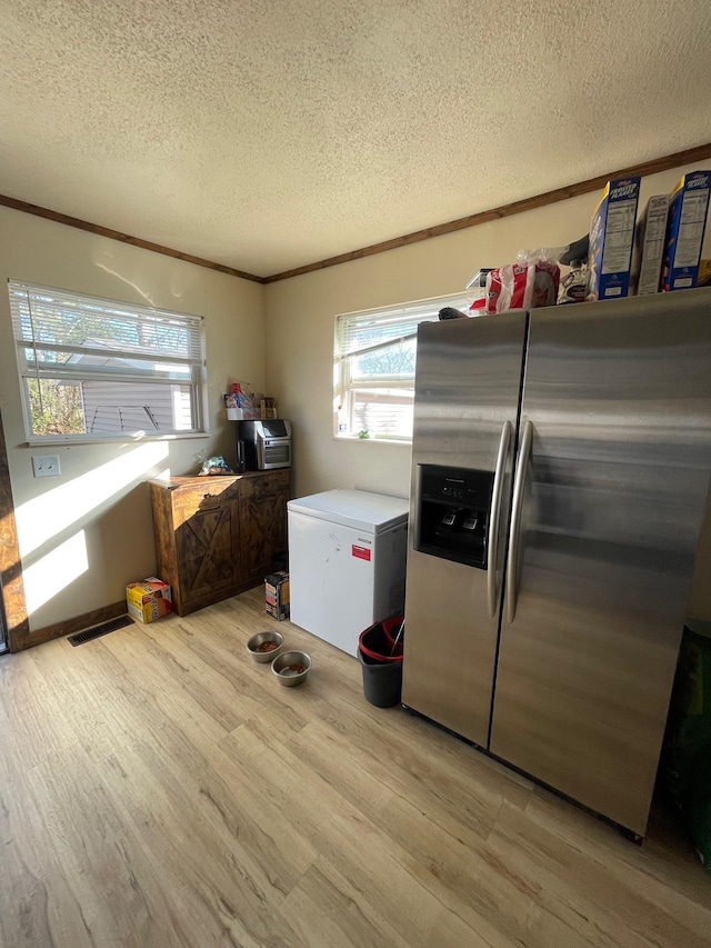 kitchen with refrigerator, stainless steel fridge, light hardwood / wood-style floors, crown molding, and a textured ceiling