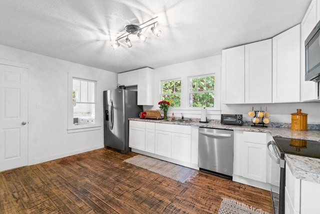 kitchen with light stone counters, dark wood-type flooring, stainless steel appliances, and white cabinets