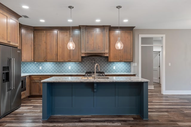 kitchen with stainless steel appliances, an island with sink, light stone countertops, and decorative light fixtures