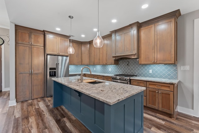 kitchen with sink, high end appliances, light stone counters, an island with sink, and decorative light fixtures