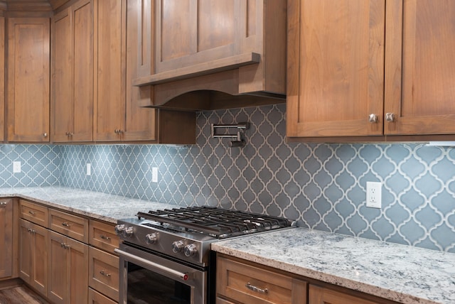 kitchen featuring light stone counters, premium range hood, decorative backsplash, and stainless steel gas range oven