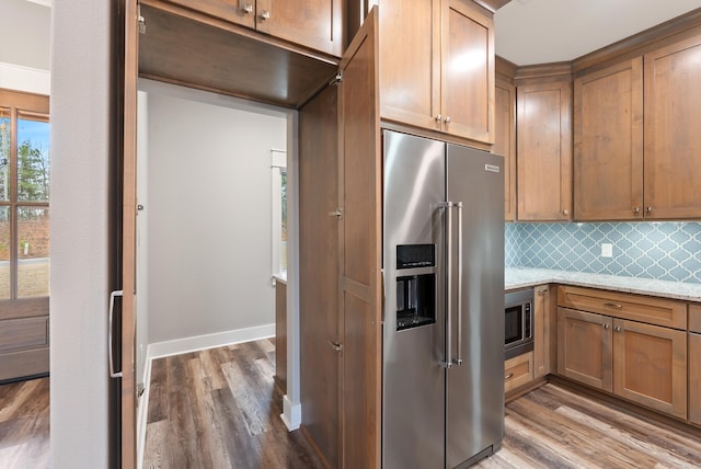 kitchen featuring stainless steel appliances, light stone countertops, hardwood / wood-style floors, and decorative backsplash