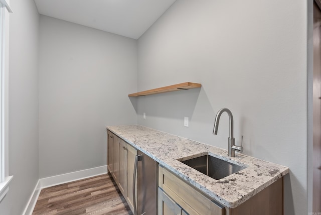 kitchen featuring light stone counters, wood-type flooring, dishwasher, and sink