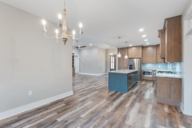 kitchen with decorative light fixtures, appliances with stainless steel finishes, light stone countertops, a kitchen island with sink, and decorative backsplash