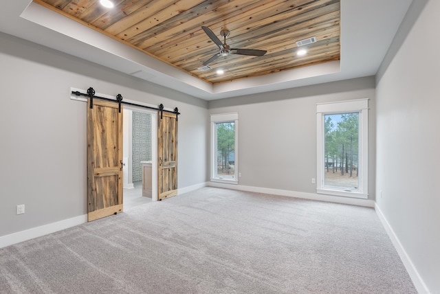 interior space with a barn door, wood ceiling, and a tray ceiling