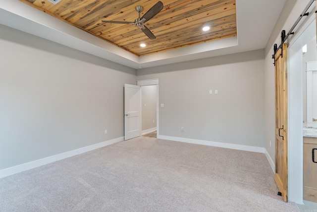 carpeted spare room with ceiling fan, wooden ceiling, a barn door, and a raised ceiling