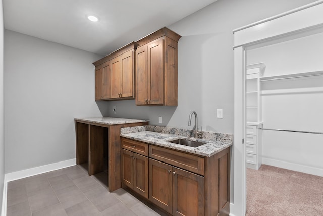 kitchen with sink, light colored carpet, and light stone counters