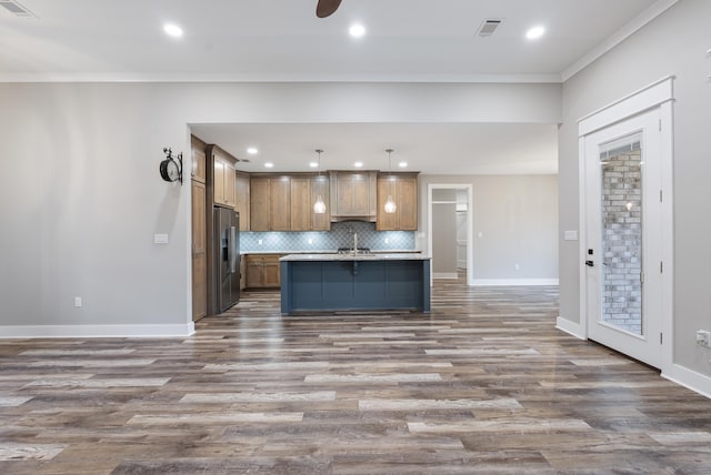 kitchen with tasteful backsplash, decorative light fixtures, high quality fridge, ornamental molding, and a kitchen island with sink