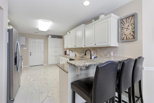 kitchen with kitchen peninsula, a breakfast bar, white cabinets, and stainless steel refrigerator with ice dispenser