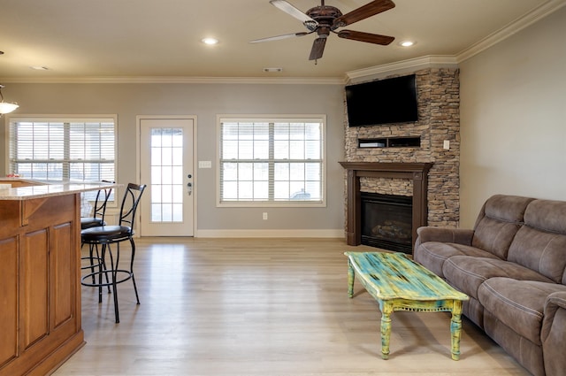 living room featuring crown molding, a stone fireplace, ceiling fan, and light hardwood / wood-style flooring