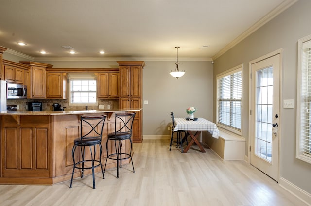 kitchen featuring tasteful backsplash, crown molding, light hardwood / wood-style floors, and hanging light fixtures