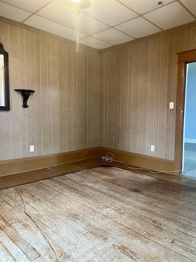 spare room with wood-type flooring, a drop ceiling, and wooden walls
