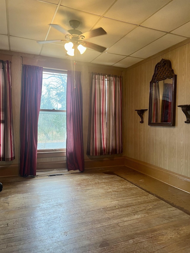spare room featuring a paneled ceiling, wood walls, ceiling fan, and light wood-type flooring
