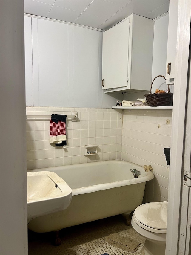 bathroom with tile walls, a tub to relax in, tile patterned flooring, and toilet