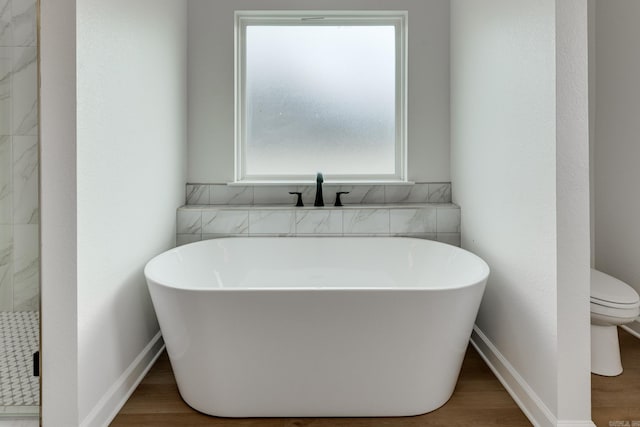 bathroom featuring hardwood / wood-style flooring, toilet, and a tub to relax in