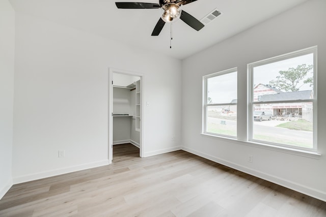 unfurnished bedroom featuring a spacious closet, light hardwood / wood-style floors, a closet, and ceiling fan