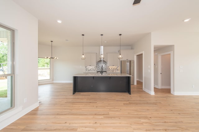 kitchen featuring tasteful backsplash, hanging light fixtures, an island with sink, and stainless steel refrigerator