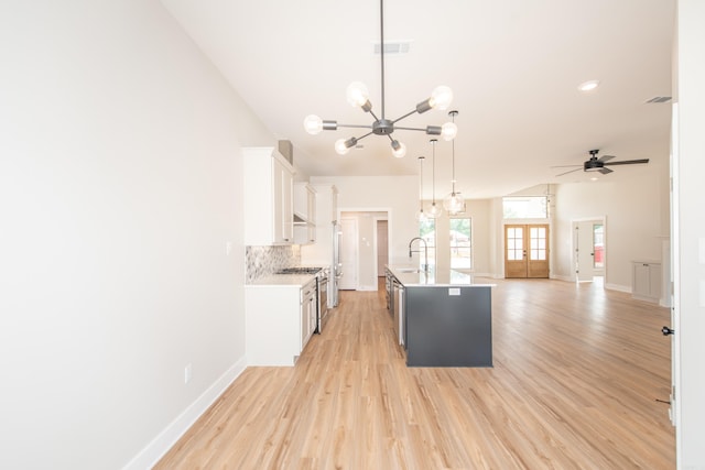 kitchen with white cabinetry, sink, decorative backsplash, hanging light fixtures, and a kitchen island with sink