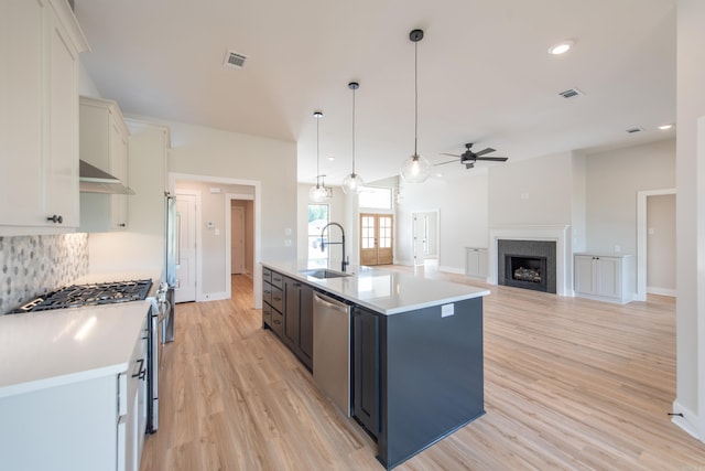 kitchen featuring appliances with stainless steel finishes, decorative light fixtures, white cabinetry, an island with sink, and sink