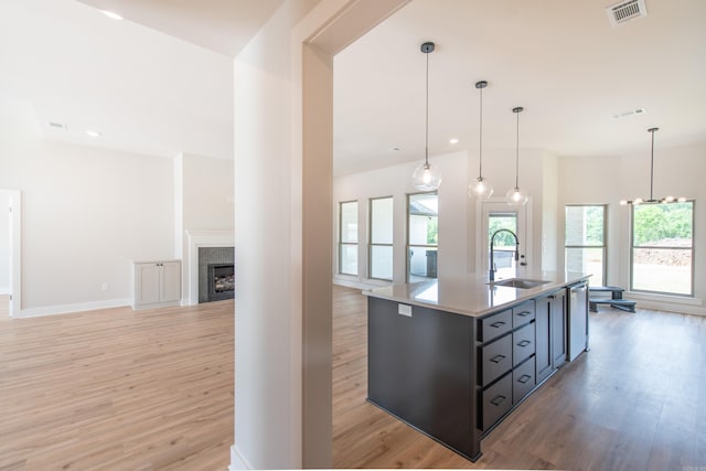 kitchen featuring an island with sink, sink, light hardwood / wood-style flooring, and decorative light fixtures