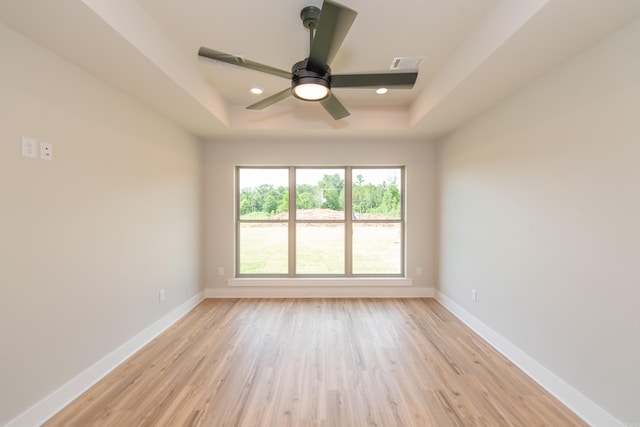 spare room featuring a raised ceiling, ceiling fan, and light wood-type flooring