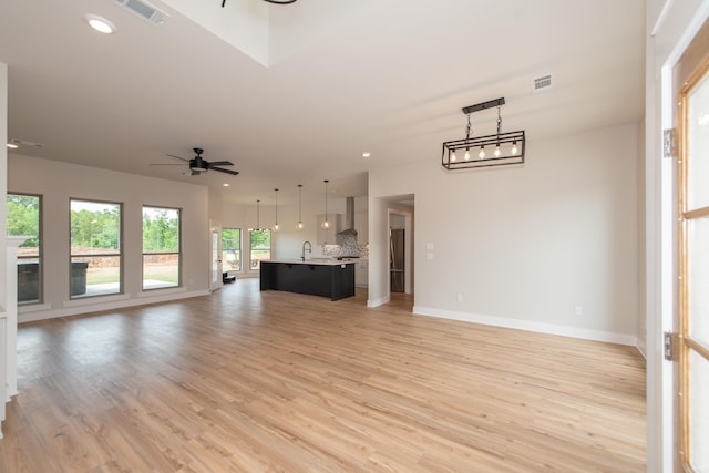 unfurnished living room with sink, ceiling fan, and light wood-type flooring