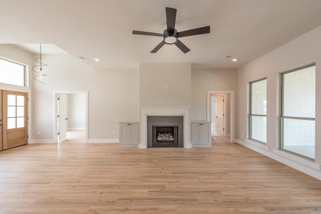 unfurnished living room featuring a tiled fireplace, a high ceiling, ceiling fan, and light hardwood / wood-style flooring