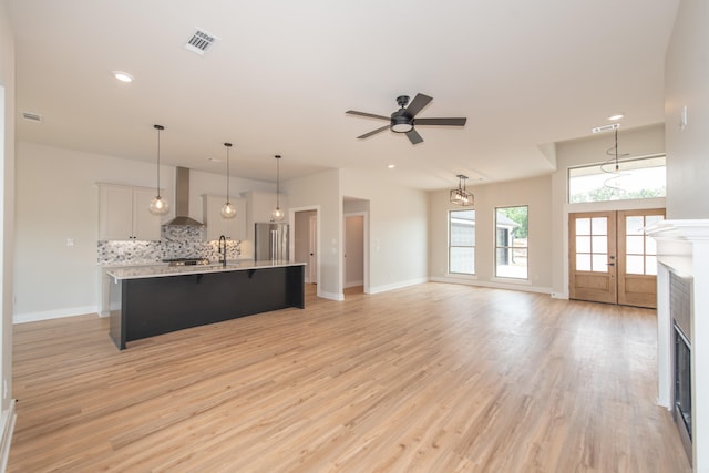 kitchen featuring wall chimney exhaust hood, white cabinetry, stainless steel fridge, pendant lighting, and a kitchen island with sink