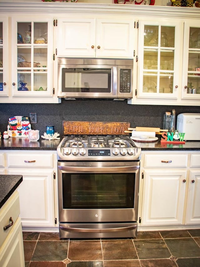 kitchen with tasteful backsplash, white cabinetry, appliances with stainless steel finishes, and dark stone counters