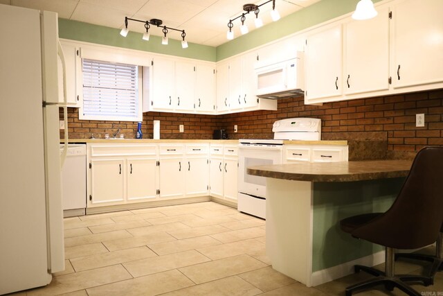 kitchen with tasteful backsplash, a breakfast bar area, white cabinets, kitchen peninsula, and white appliances