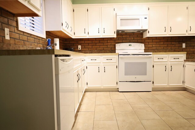 kitchen with white cabinetry, light tile patterned floors, white appliances, and brick wall