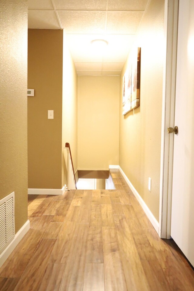 hall with a drop ceiling and light wood-type flooring