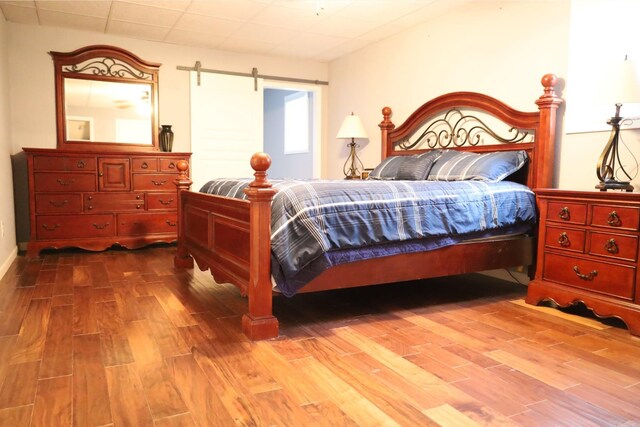 bedroom with hardwood / wood-style flooring, a barn door, and a drop ceiling