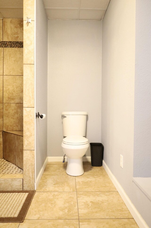 bathroom with a drop ceiling, tile patterned floors, toilet, and tiled shower