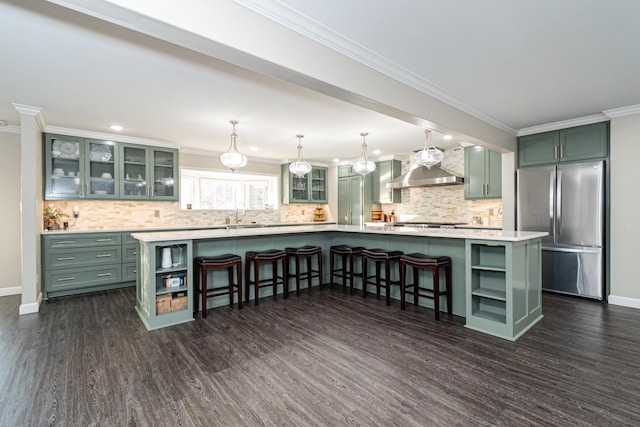 kitchen featuring wall chimney range hood, crown molding, stainless steel fridge, green cabinetry, and a kitchen island