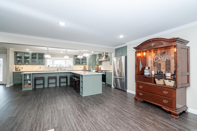 kitchen featuring a breakfast bar area, decorative light fixtures, a kitchen island, stainless steel appliances, and wall chimney range hood